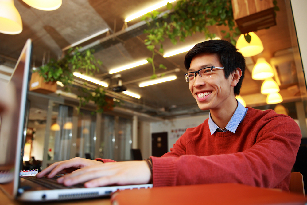 Gai homme asiatique portant des lunettes en tapant sur un ordinateur portable dans un café