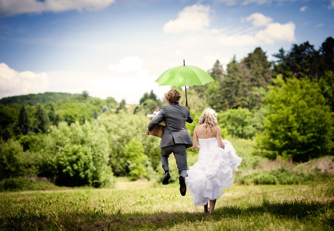 Les mariés qui traversent le champ avec un parapluie