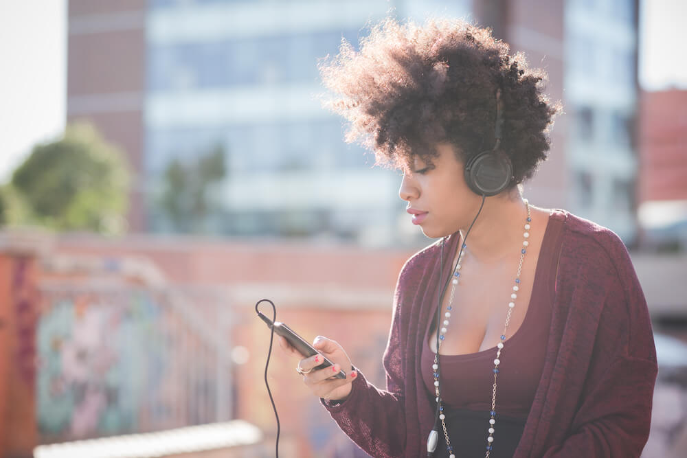 femme noire écoutant un podcast au casque en marchant dans la ville
