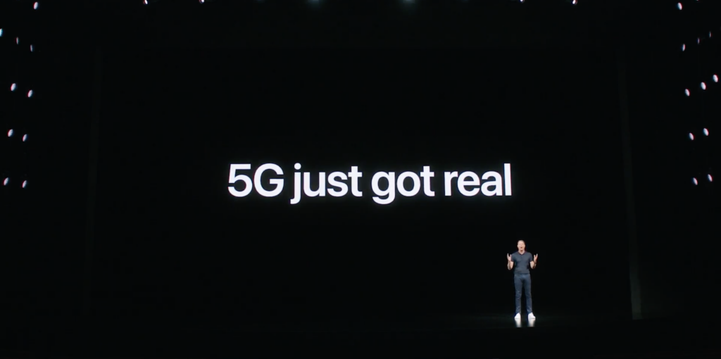 Un gars debout sur une scène noire avec 5G vient de s'afficher sur un écran derrière
