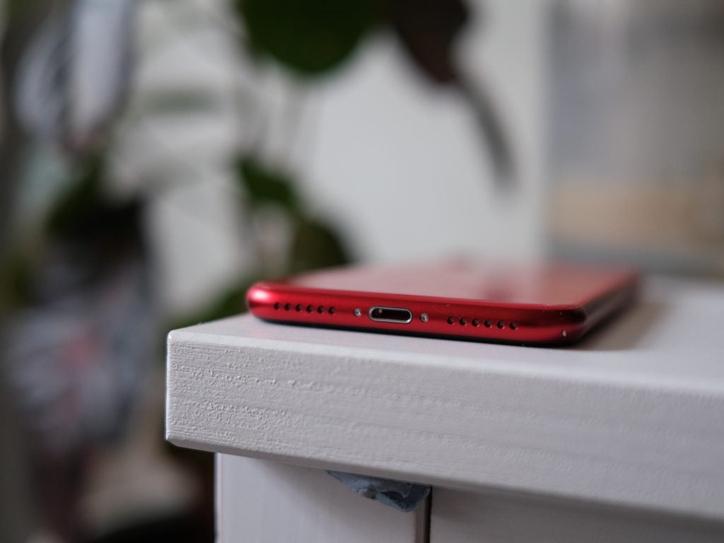 Vue du bord inférieur d'un iPhone SE rouge placé à l'envers sur une étagère blanche