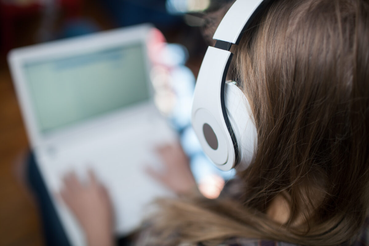 Image prise par-dessus l'épaule d'une femme portant des écouteurs et travaillant sur un ordinateur portable.  musique de fond vlog