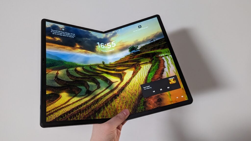 Main tenant le Lenovo ThinkPad X1 Fold avec un papier peint paysage.